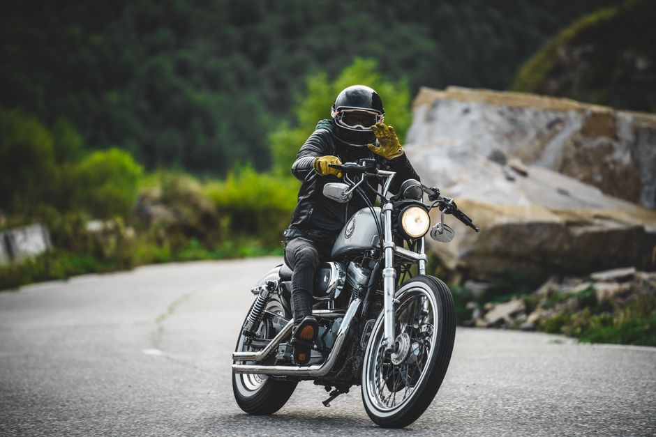 A motorcyclist wearing protective gear waves while riding on a winding mountain road.
