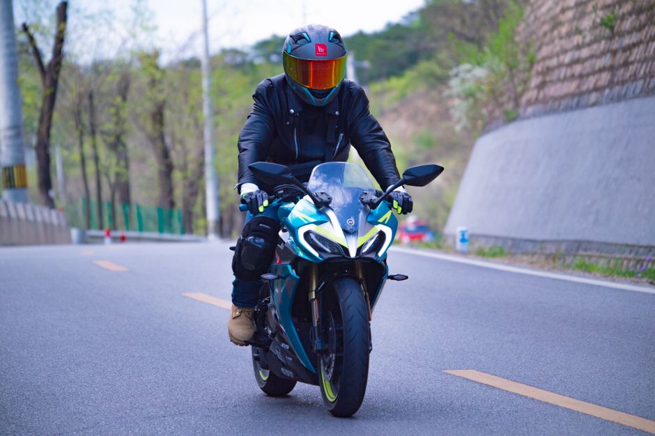 Unrecognizable motorcyclist wearing black gear and helmet rides a sportbike on a scenic road.