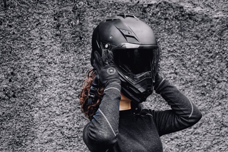 A woman in gloves putting on a motorcycle helmet against a textured background, highlighting safety and adventure.